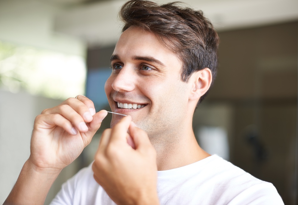 A man flosses his teeth as part of his daily oral hygiene routine, supporting the results of professional dental cleanings and preventing gum disease. – Dental Cleaning in Torrance CA