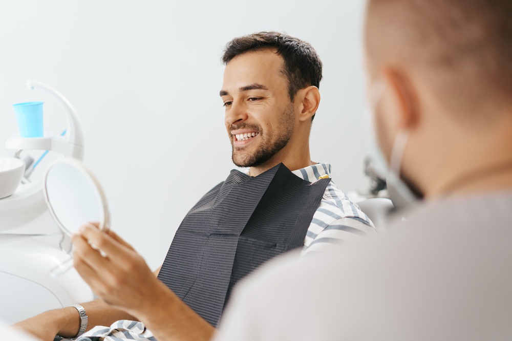 A male patient smiling while looking in a mirror after dental treatment, showcasing cosmetic and restorative dentistry results – Dentist in Redondo Beach.