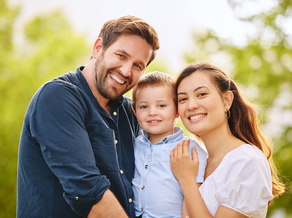 A smiling mother, father, and young son pose together outdoors, showcasing bright and healthy smiles supported by quality family dental care - Dentist in San Pedro CA