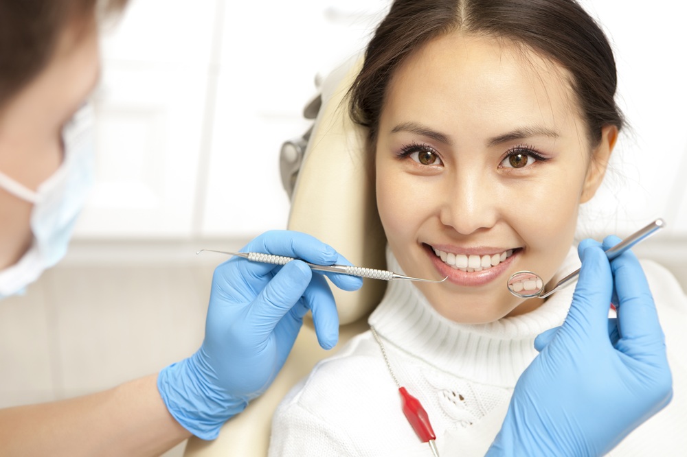 A patient smiling during a dental exam while instruments are used to assess her oral health – Dentist in Torrance CA.