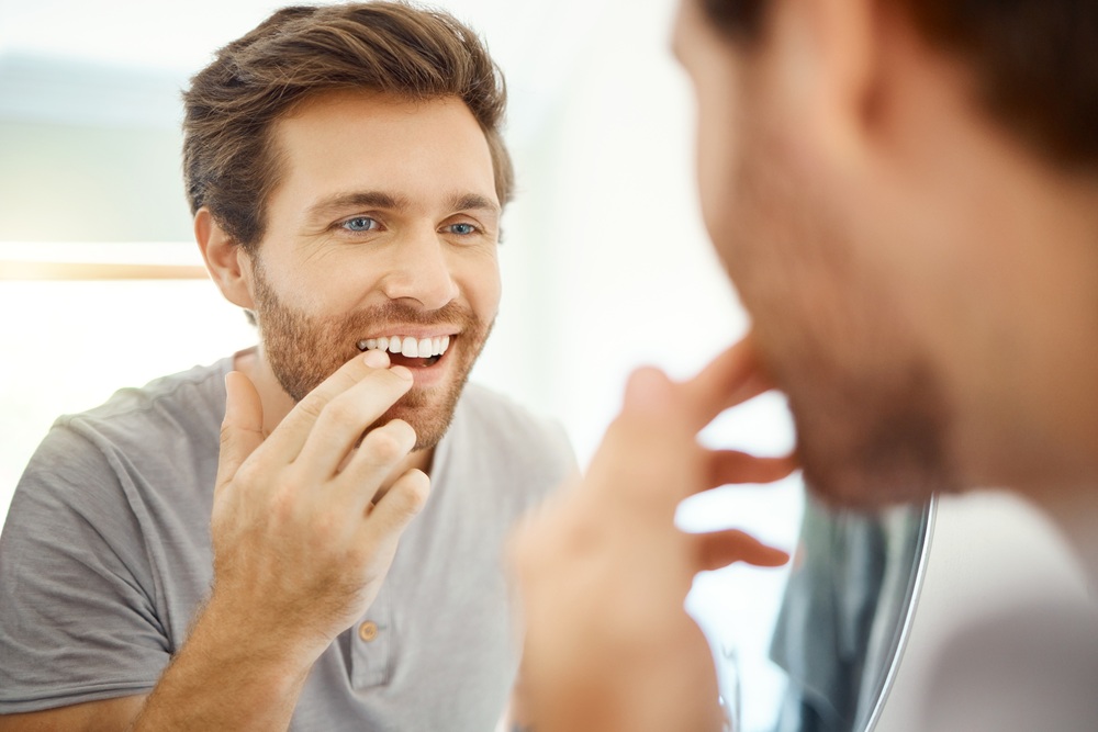 A man examines his smile in the mirror after a thorough dental cleaning, highlighting improved oral health and refreshed, polished teeth. – Dental Cleaning in Torrance CA